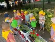 Grupa dzieci podlewa rośliny posadzone w skrzynkach udekorowanych w formie pociągu