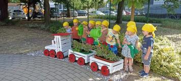 Pociąg ze skrzynek po owocach z zasadzonymi roślinami, w tle grupa dzieci
