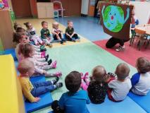 Grupa dzieci siedząc na podłodze ogląda plakat z planetą Ziemią